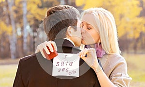 Love, relationships, engagement and wedding concept - man proposes a woman to marry, red box ring, happy romantic couple kissing