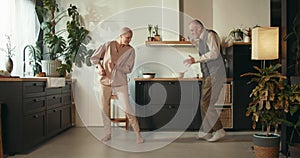 LOVE AND RELATIONSHIPS. Idyllic happy sweet elderly 65-70 senior couple have fun dancing together in cozy house kitchen.