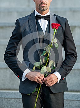 love rendezvous concept. cropped view of tuxedo man with love rose. flower present for love day