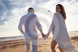 Love, romance on the beach. Young beautiful couple, woman, man, in white loose flying clothes, walk, along the seashore.