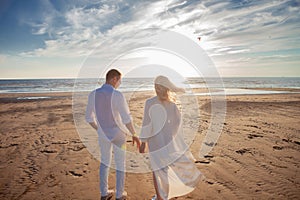 Love, romance on the beach. Young beautiful couple, woman, man, in white loose flying clothes, walk, along the seashore.