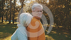 Love and romance at old age. Retired couple enjoying autumn day in forest staying back to back and smiling