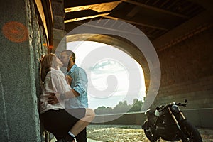 Love and romantic concept. Couple in love with sunset stand by the wall kiss and hug under the bridge next to motorcycle