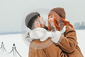 Love romantic couple lovestory. Brutal bearded man, bright red-haired girl woman in winter park. Romantic date, kissing photo