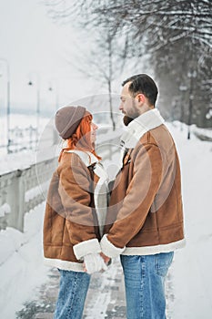 Love romantic couple lovestory. Brutal bearded man, bright red-haired girl woman in winter park. Romantic date, kissing