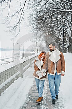 Love romantic couple lovestory. Brutal bearded man, bright red-haired girl woman in winter park. Romantic date, kissing