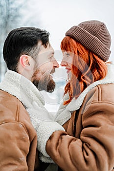 Love romantic couple lovestory. Brutal bearded man, bright red-haired girl woman in winter park. Romantic date, kissing