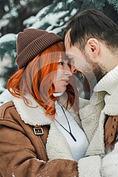 Love romantic couple lovestory. Brutal bearded man, bright red-haired girl woman in winter park. Romantic date, kissing