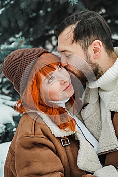 Love romantic couple lovestory. Brutal bearded man, bright red-haired girl woman in winter park. Romantic date, kissing