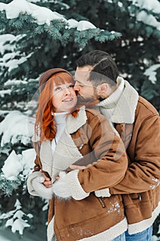 Love romantic couple lovestory. Brutal bearded man, bright red-haired girl woman in winter park. Romantic date, kissing