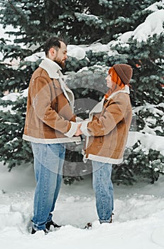 Love romantic couple lovestory. Brutal bearded man, bright red-haired girl woman in winter park. Romantic date, kissing