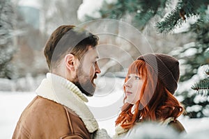 Love romantic couple lovestory. Brutal bearded man, bright red-haired girl woman in winter park. Romantic date, kissing
