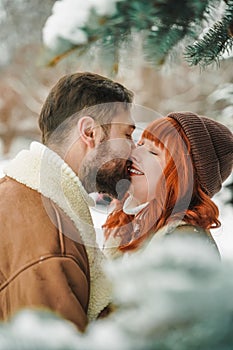 Love romantic couple lovestory. Brutal bearded man, bright red-haired girl woman in winter park. Romantic date, kissing