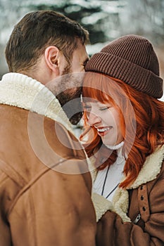 Love romantic couple lovestory. Brutal bearded man, bright red-haired girl woman in winter park. Romantic date, kissing