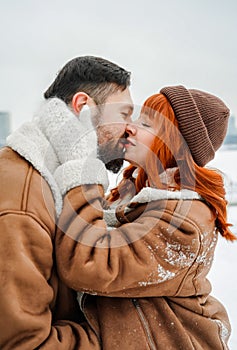 Love romantic couple lovestory. Brutal bearded man, bright red-haired girl woman in winter park. Romantic date, kissing