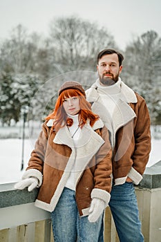 Love romantic couple lovestory. Brutal bearded man, bright red-haired girl woman in winter park. Romantic date, kissing