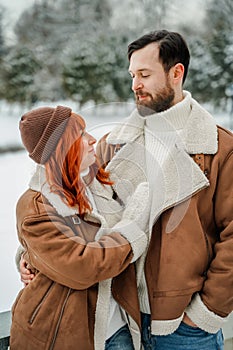 Love romantic couple lovestory. Brutal bearded man, bright red-haired girl woman in winter park. Romantic date, kissing