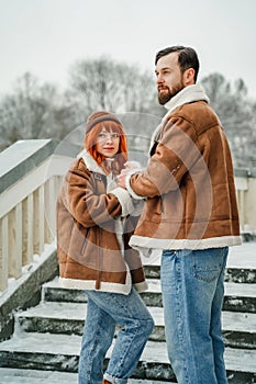 Love romantic couple lovestory. Brutal bearded man, bright red-haired girl woman in winter park. Romantic date, kissing