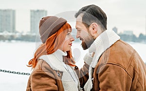 Love romantic couple lovestory. Brutal bearded man, bright red-haired girl woman in winter park. Romantic date, kissing