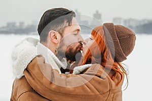 Love romantic couple lovestory. Brutal bearded man, bright red-haired girl woman in winter park. Romantic date, kissing