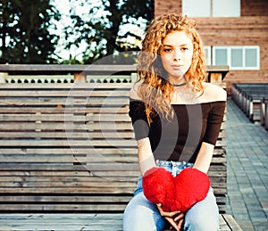 Love, sadness and loneliness. Beautiful long-haired girl in sad loneliness summer evening. She is holding a big red