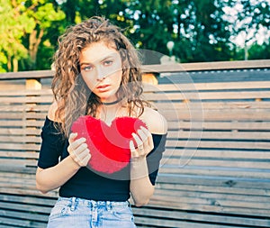 Love, sadness and loneliness. Beautiful long-haired girl in sad loneliness summer evening. She is holding a big red