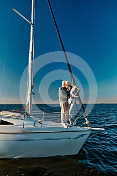 In love with the sea. Full length of beautiful senior couple standing on the side of sail boat or yacht deck floating in