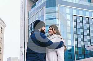 Love story of couple walking in city. Young business man in a blue jacket with a beard. And a cute woman in long coat