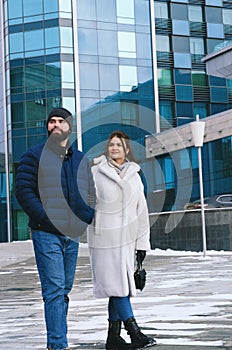 Love story of couple walking in city. Young business man in a blue jacket with a beard. And a cute woman in long coat