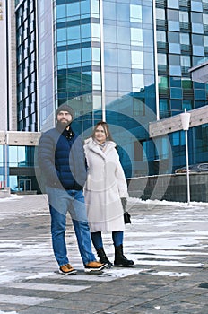 Love story of couple walking in city. Young business man in a blue jacket with a beard. And a cute woman in long coat