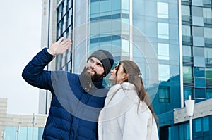 Love story of couple walking in city. Young business man in a blue jacket with a beard. And a cute woman in long coat