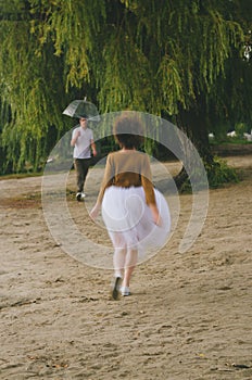 Love story of funny couple walking near river in hard rainfall with umbrella. cute man and woman in white skirt, yellow sweater