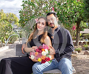 Love story. A man and a woman are hugging sitting on a bench in nature in a blooming garden. With a bouquet of flowers.