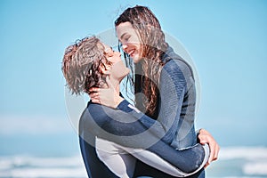 Love, surf and summer with a couple hugging on the beach with the sea or ocean in the background after surfing. Romantic