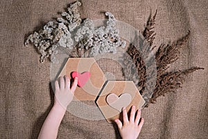 Love and sustainable living concept. Child`s hands putting crafted hearts on composition of dried flowers with two hexagon frame