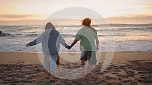 Love teenagers running sandy beach evening back view. Carefree couple enjoying