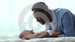 Love and tenderness. Caring african american father playing with his newborn baby, lying on bed at home, empty space