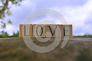 Love text on wooden block on top of big stone with blue sky background