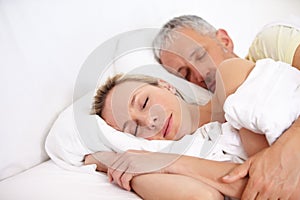 Love, tired and mature couple sleeping in bed for cuddling together on weekend morning at home. Calm, peaceful and man