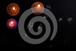 Love triangle and broken relationship concept. Wedding rings, broken glass  and three burning candles on black background