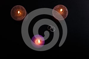 Love triangle and broken relationship concept. Wedding rings and three burning candles on black background.