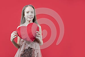 Love. Valentine`s day. A cute girl holding a red heart in her hands on a red background. Declaration of love. Congratulations on