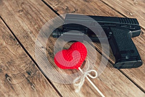 Love and violence concept: pistol gun and love red heart on wood
