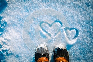 Love winter concept- feet in snow boots and heart in nature