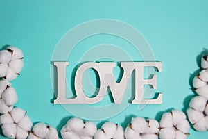 A love wooden letter with cotton flowers over the mint background.