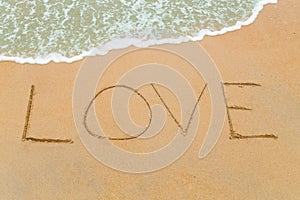 LOVE word drawn on sandy beach with wave approaching