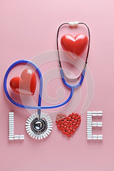 LOVE word made from medicine pills, red heart shape and stethoscope, on pink background.
