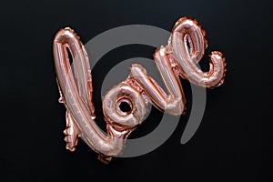 Love word from pink inflatable balloon on black background. The concept of romance, Valentine`s Day. Love rose gold foil balloon