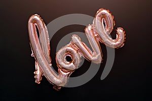 Love word from pink inflatable balloon on black background. The concept of romance, Valentine`s Day. Love rose gold foil balloon