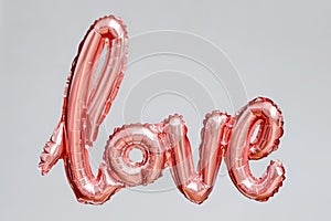 Love word from pink inflatable balloon floating in the air on grey background. The concept of romance, Valentine`s Day. Love rose